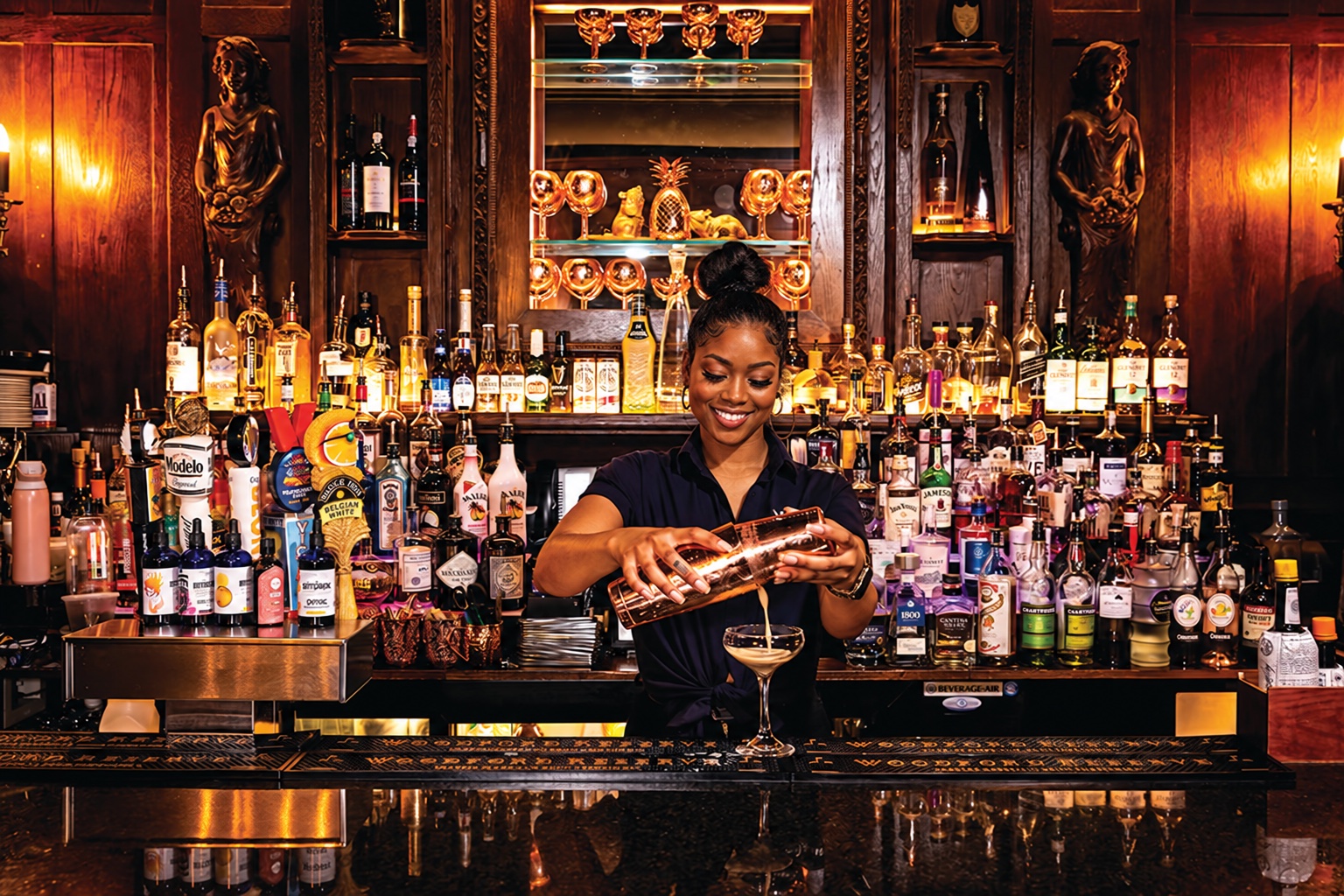 A bartender pouring a cocktail at The Manor’s warmly lit bar